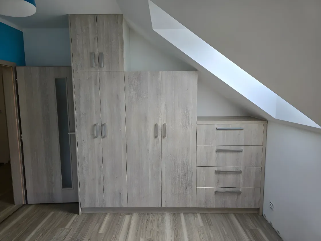 Skříně v&nbsp;dekoru dubu pod šikmým stropem s&nbsp;šuplíky a&nbsp;zkosenými dvířky
