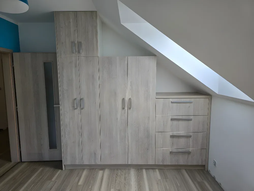 Skříně v&nbsp;dekoru dubu pod šikmým stropem s&nbsp;šuplíky a&nbsp;zkosenými dvířky