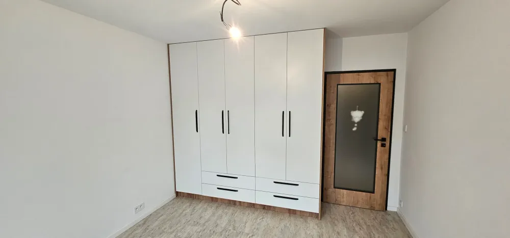 Bílá šatní skříň s&nbsp;pěti dveřmi a&nbsp;zásuvkami vedle vchodových dveří