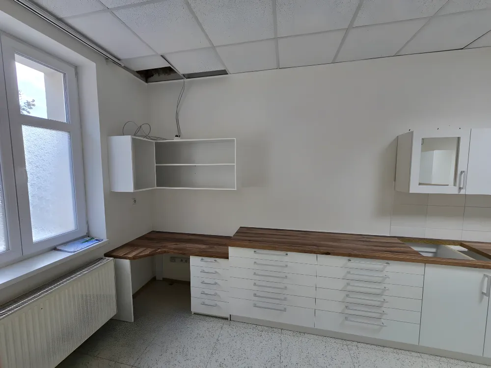 Dlouhá bílá sestava zásuvek s&nbsp;dřevěnou deskou pod okny a&nbsp;závěsné skříňky