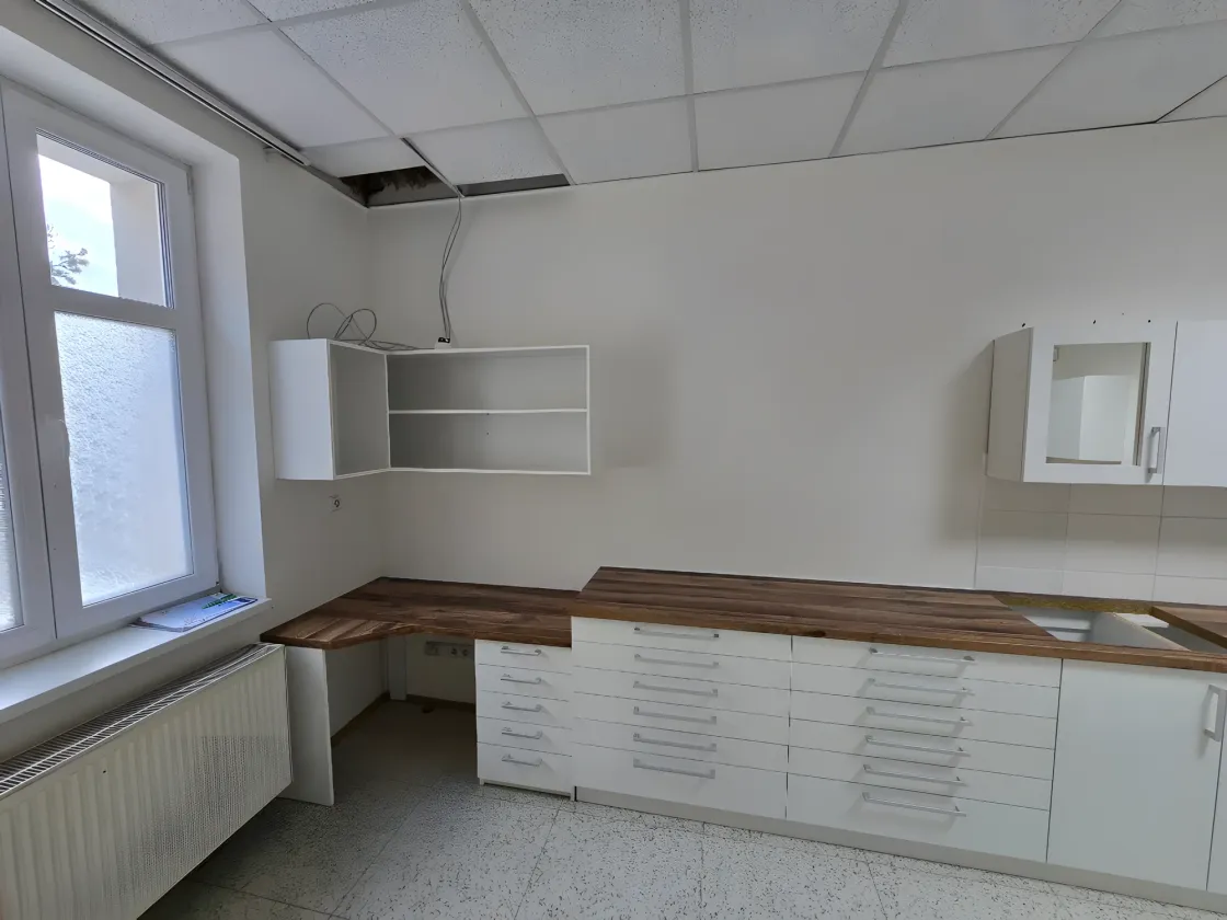 Dlouhá bílá sestava zásuvek s&nbsp;dřevěnou deskou pod okny a&nbsp;závěsné skříňky