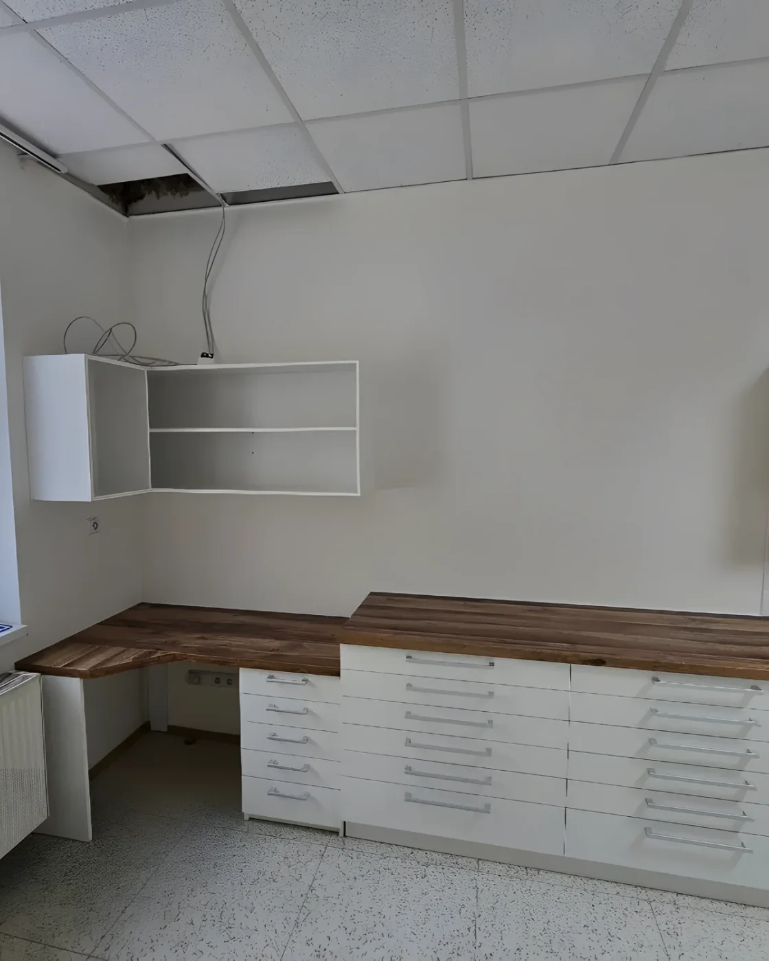 Dlouhá bílá sestava zásuvek s&nbsp;dřevěnou deskou pod okny a&nbsp;závěsné skříňky