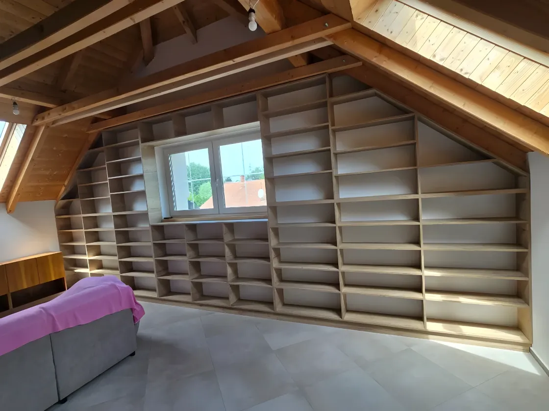 Rozsáhlá knihovna pod šikmým trámovým stropem kolem okna