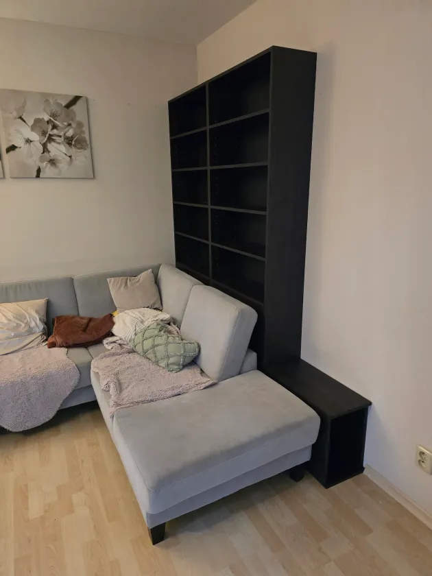 Černý vysoký regál s&nbsp;policemi za šedou sedačkou