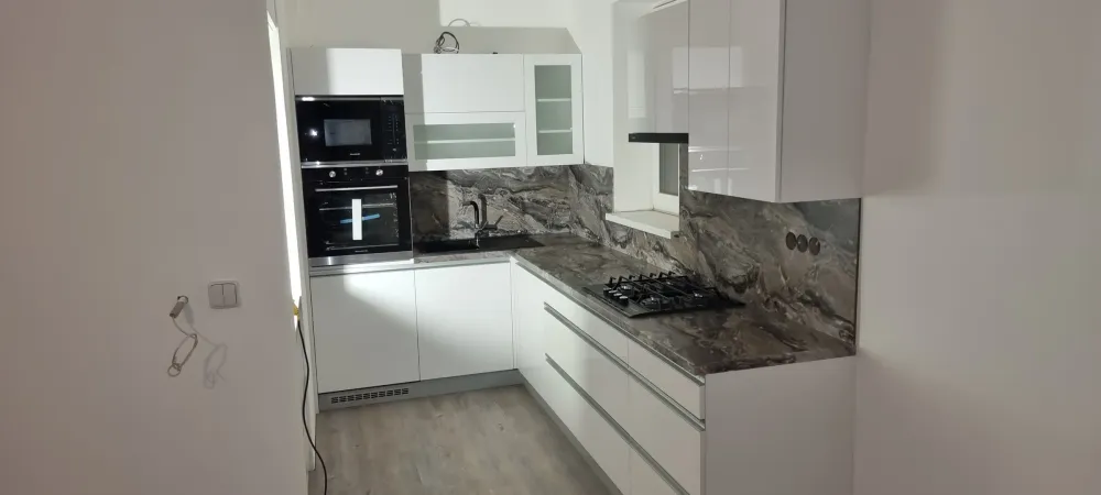 Bílá linka s&nbsp;mramorovým obkladem, vestavnými spotřebiči a&nbsp;prosklenými horními skříňkami