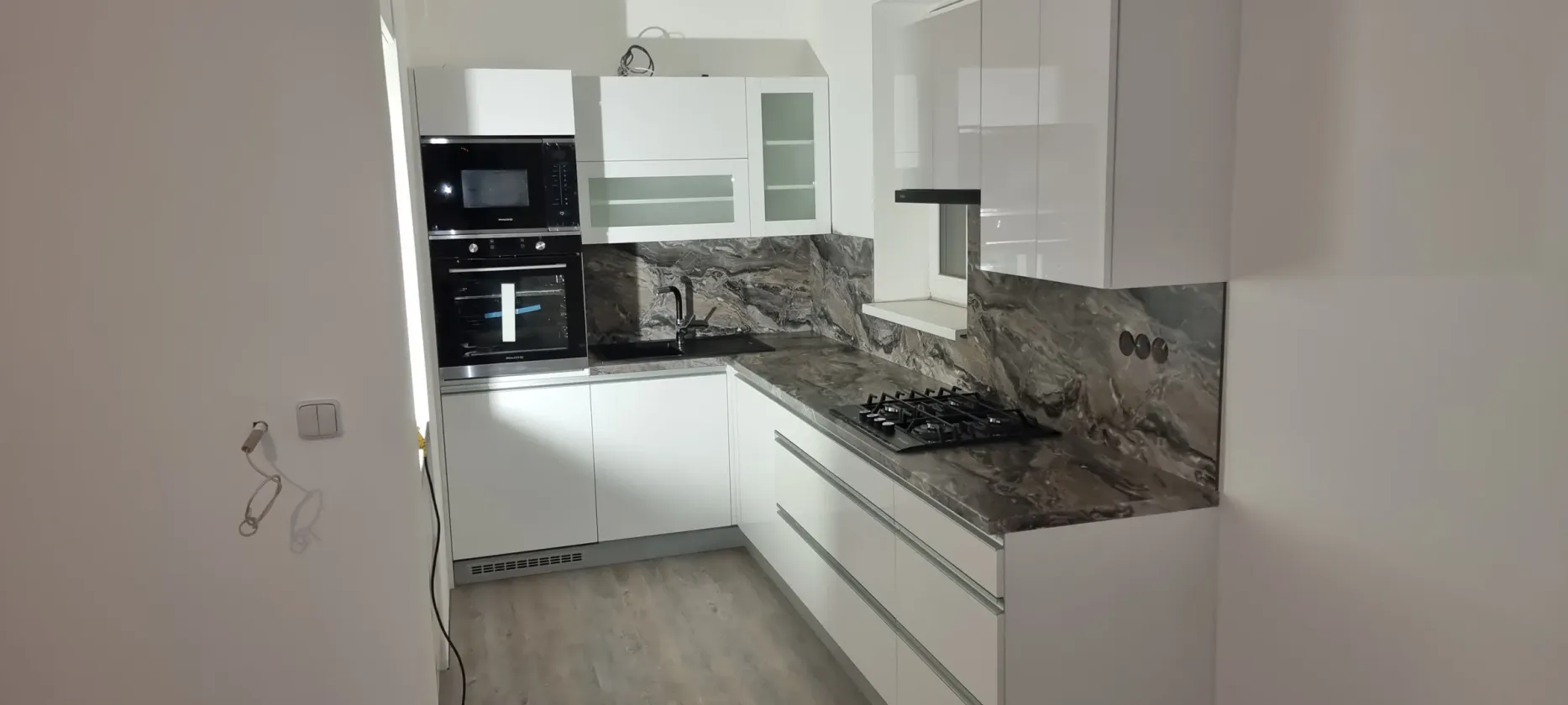 Bílá linka s&nbsp;mramorovým obkladem, vestavnými spotřebiči a&nbsp;prosklenými horními skříňkami