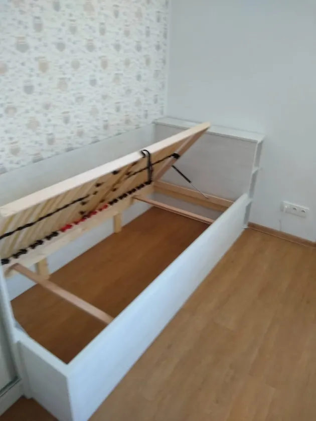 Bílá jednolůžková postel s&nbsp;vyklopeným roštem a&nbsp;úložným prostorem pod ním