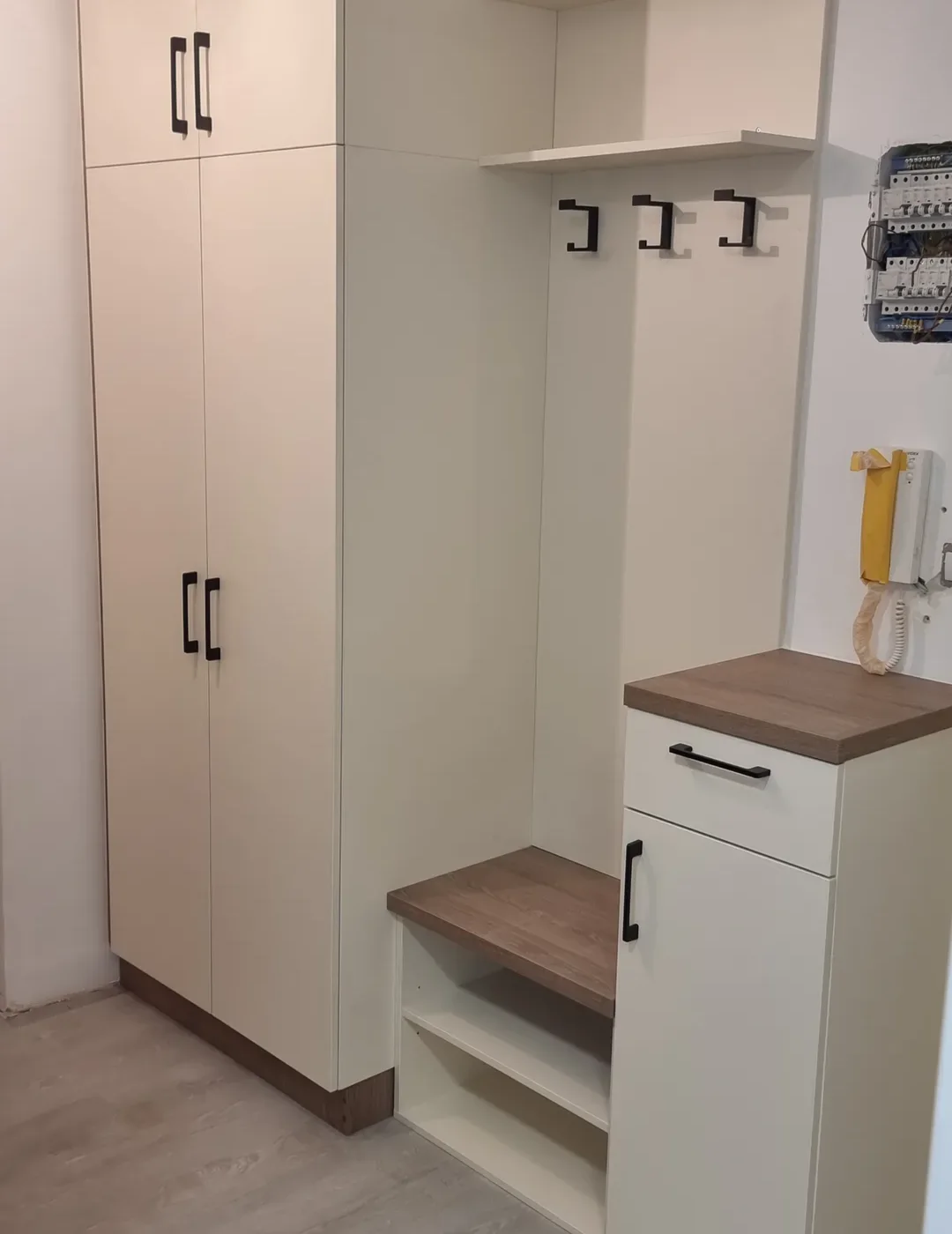 Bílá předsíň s&nbsp;vysokou skříní, věšáky nad lavicí a&nbsp;botníkem