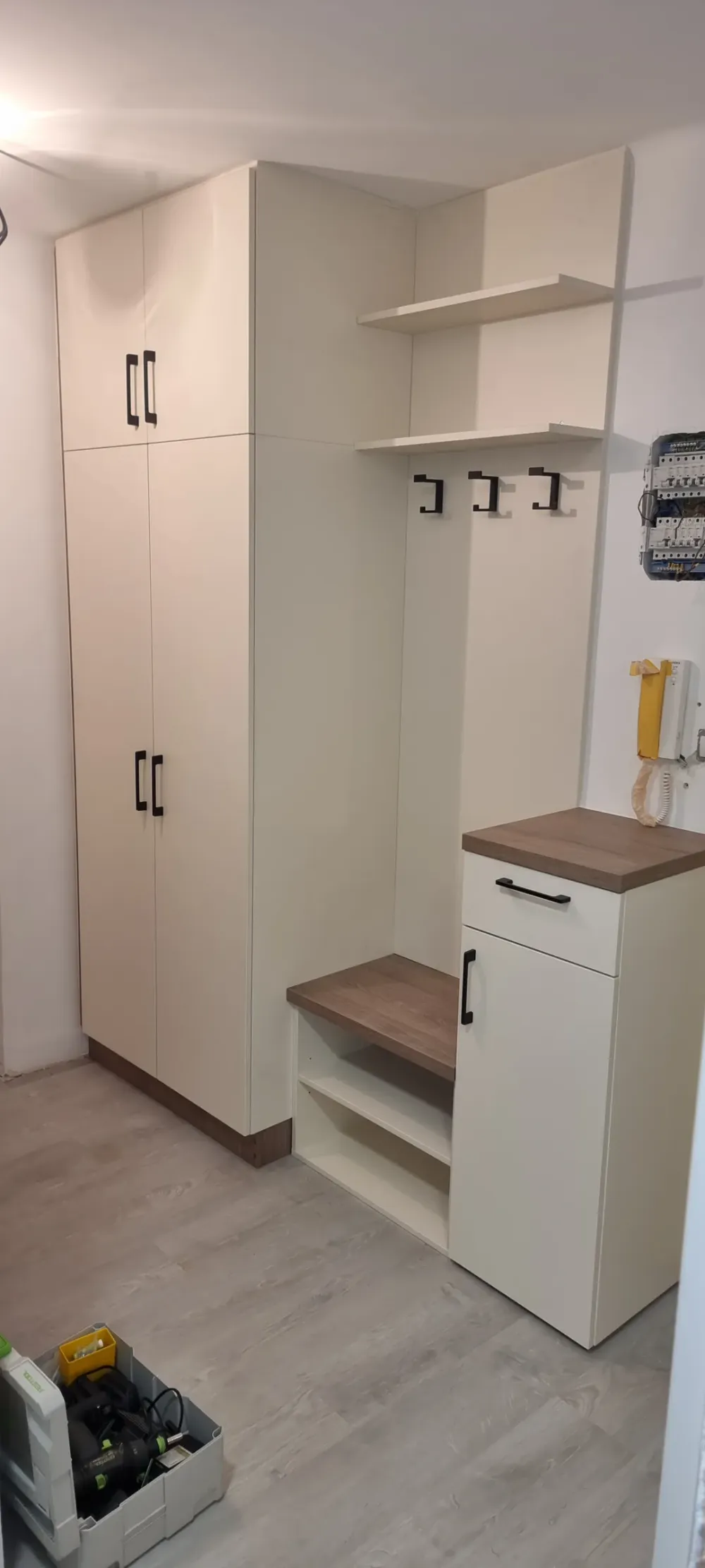 Bílá předsíň s&nbsp;vysokou skříní, věšáky nad lavicí a&nbsp;botníkem