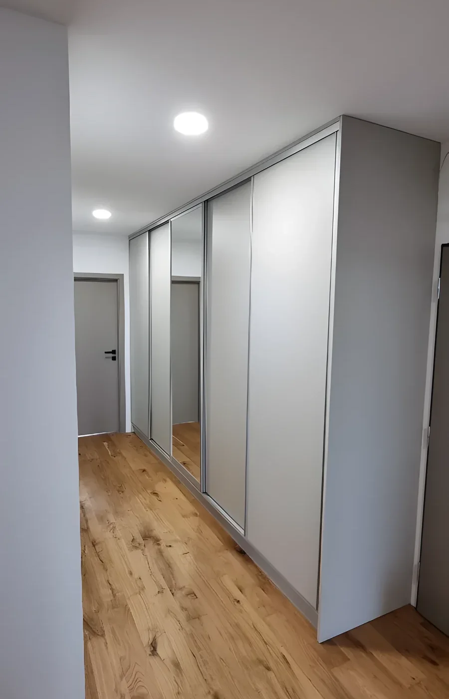 Bílá posuvná skříň přes celou chodbu s&nbsp;dubovou podlahou