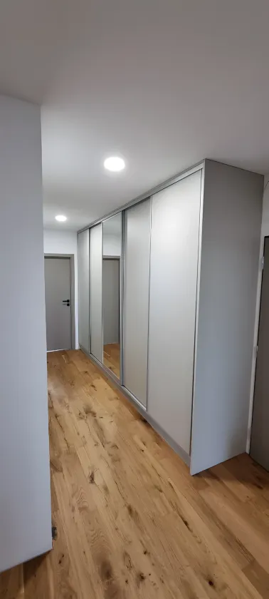 Bílá posuvná skříň přes celou chodbu s&nbsp;dubovou podlahou