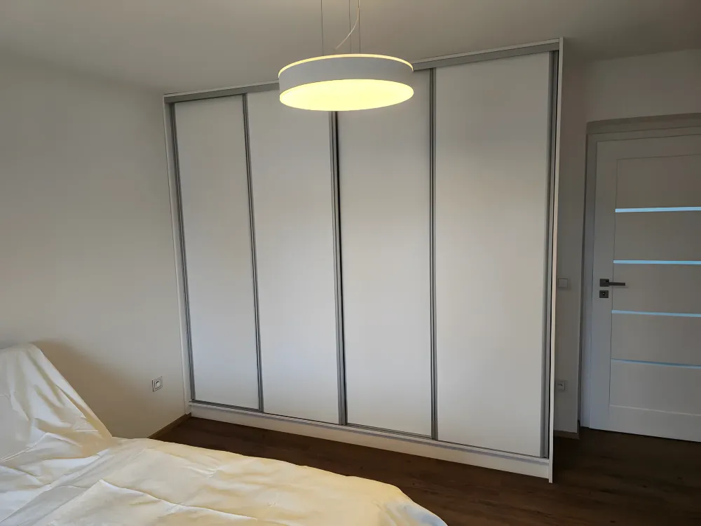 Bílá posuvná skříň se čtyřmi dveřmi v&nbsp;ložnici