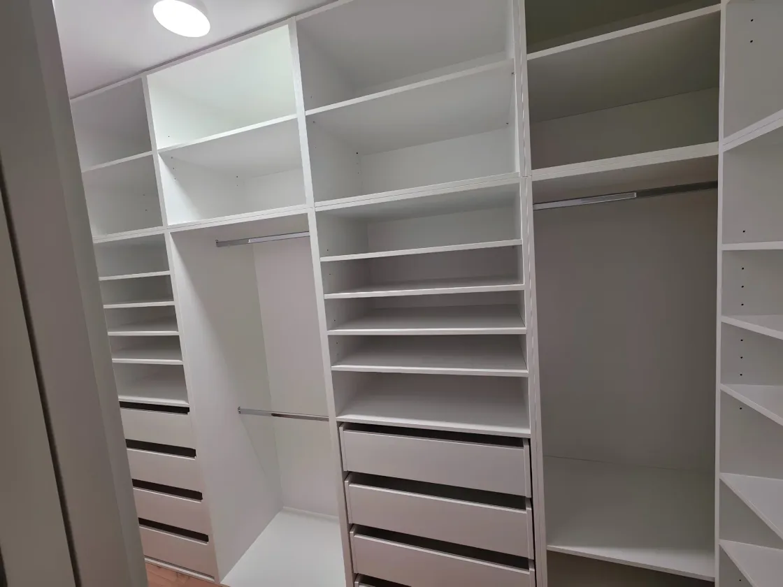 Šatna se třemi stěnami bílých polic, tyčí na ramínka a&nbsp;zásuvek