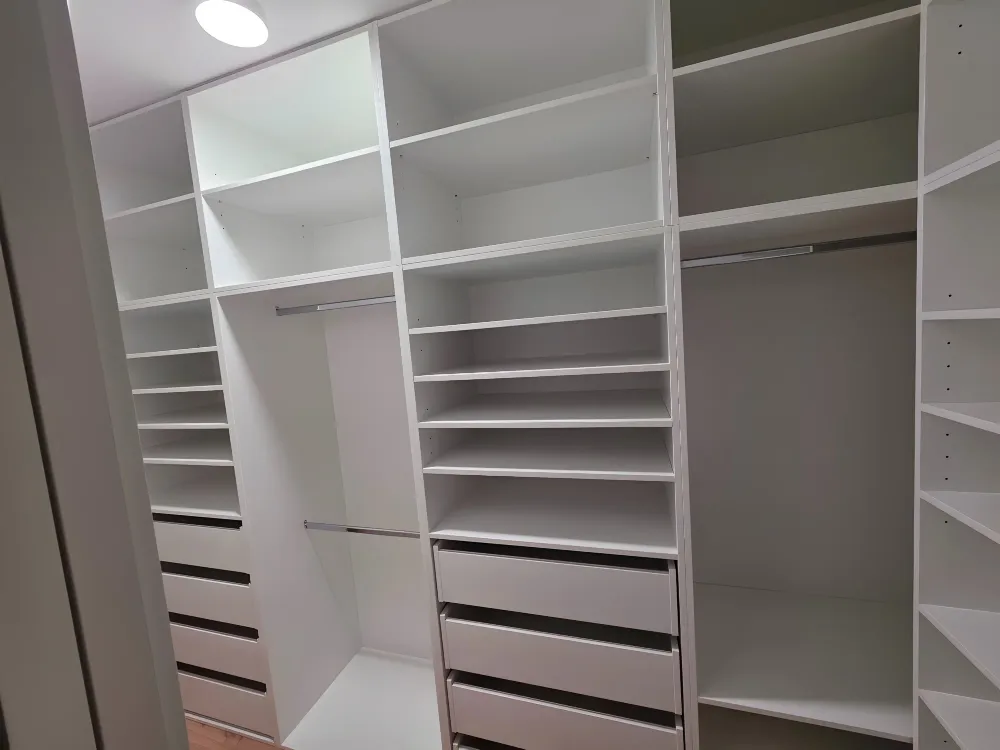 Šatna se třemi stěnami bílých polic, tyčí na ramínka a&nbsp;zásuvek