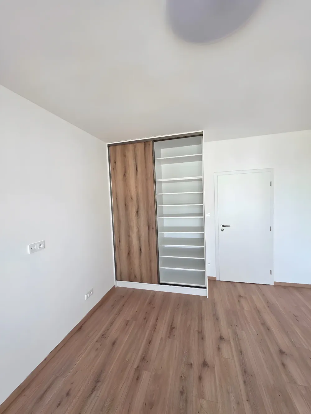 Vestavěná skříň s&nbsp;posuvnými dveřmi v&nbsp;dekoru dubu a&nbsp;bílým korpusem v&nbsp;ložnici