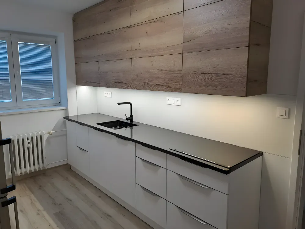 Dubové horní skříňky nad bílou linkou s&nbsp;černou deskou a&nbsp;LED
