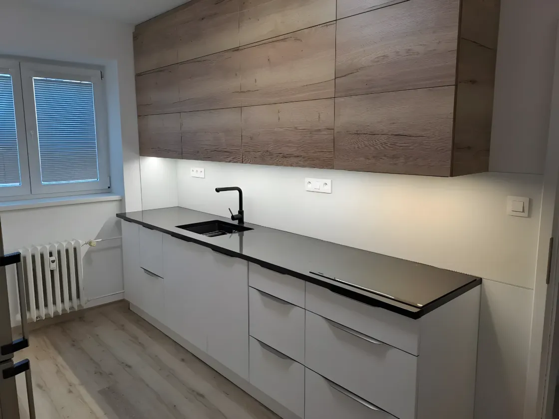 Dubové horní skříňky nad bílou linkou s&nbsp;černou deskou a&nbsp;LED