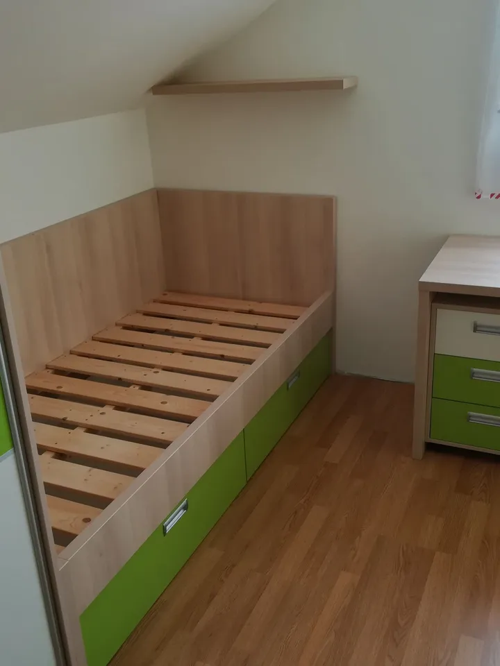 Dětský pokoj v&nbsp;podkroví: postel se zelenými šuplíky a&nbsp;skříň pod šikminou