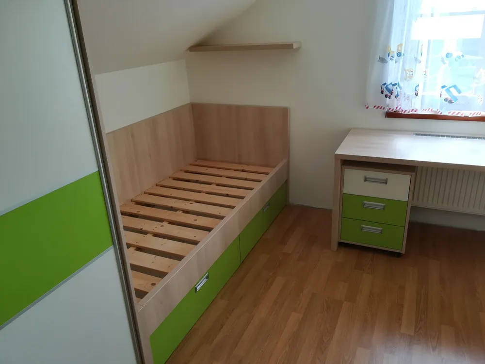 Postel s&nbsp;šuplíky pod šikmou stěnou a&nbsp;zelenými čely a&nbsp;skříní