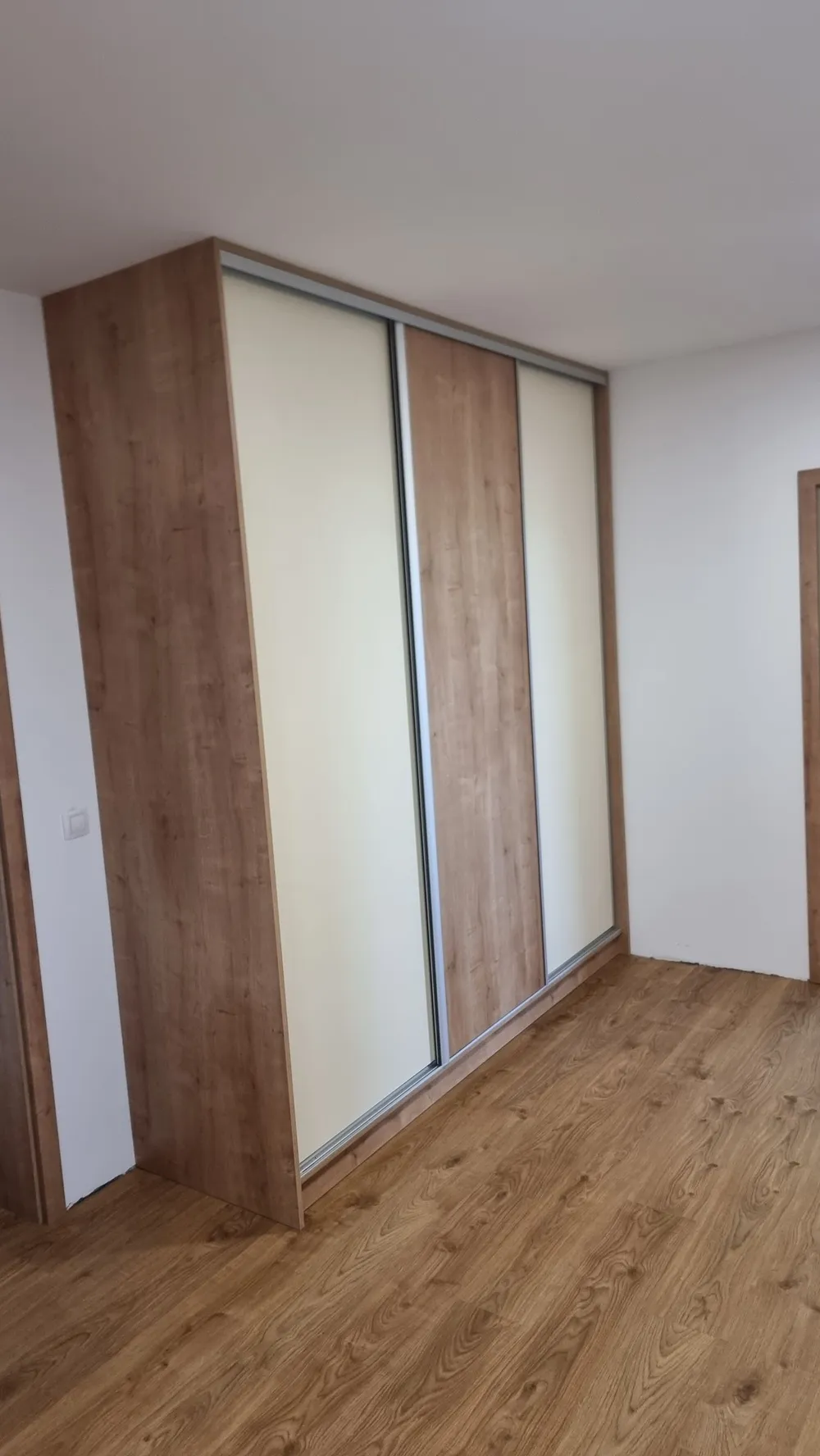 Posuvná skříň s&nbsp;bílými a&nbsp;dubovými panely v&nbsp;rohu místnosti