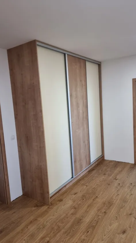 Posuvná skříň s&nbsp;bílými a&nbsp;dubovými panely v&nbsp;rohu místnosti